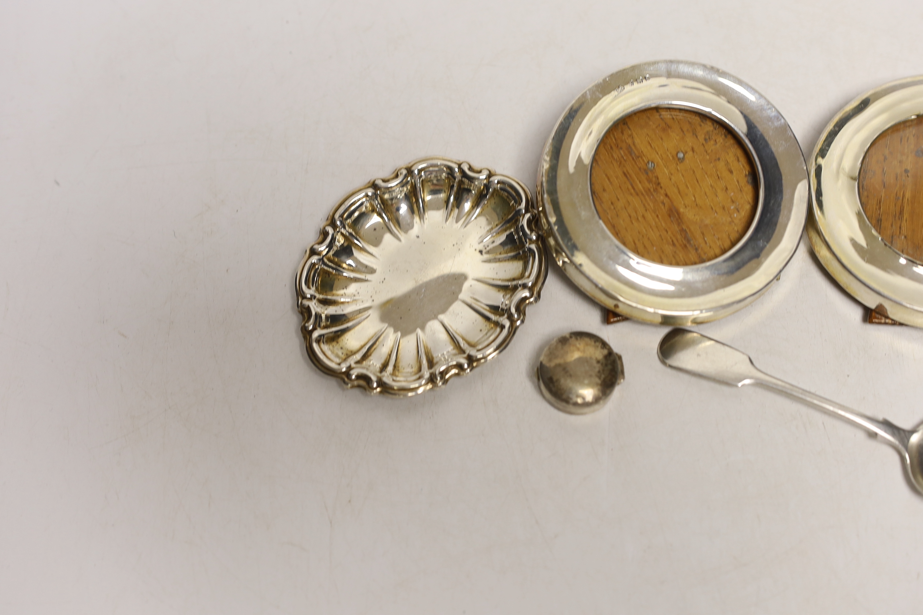 A small pair of George V silver mounted circular photograph frames, London, 1921, 75mm and four other items including a silver pill box and condiment spoon and small frame.